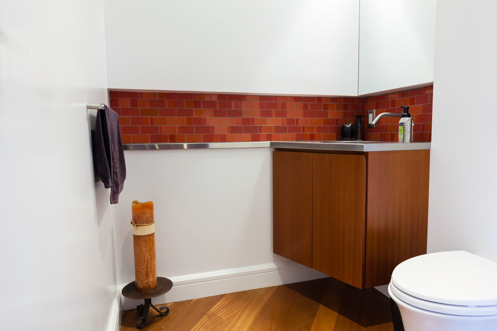 Свежая идея для дизайна: туалет в современном стиле с плоскими фасадами, темными деревянными фасадами, инсталляцией, красной плиткой, керамической плиткой, белыми стенами, паркетным полом среднего тона, монолитной раковиной и столешницей из нержавеющей стали - отличное фото интерьера