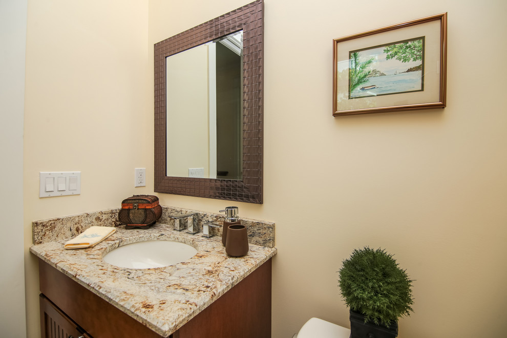 Small island style powder room photo in Miami with flat-panel cabinets, dark wood cabinets, a one-piece toilet, beige walls, an undermount sink and granite countertops