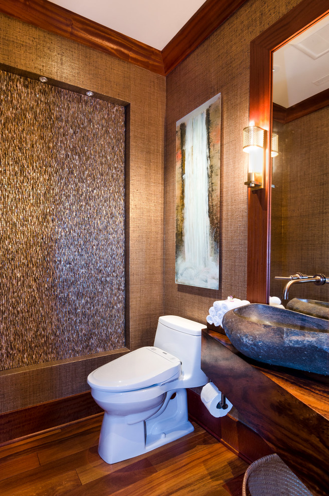 Foto på ett litet tropiskt toalett, med öppna hyllor, en toalettstol med hel cisternkåpa, beige kakel, mellanmörkt trägolv, ett fristående handfat, träbänkskiva, skåp i mellenmörkt trä, mosaik, bruna väggar och brunt golv