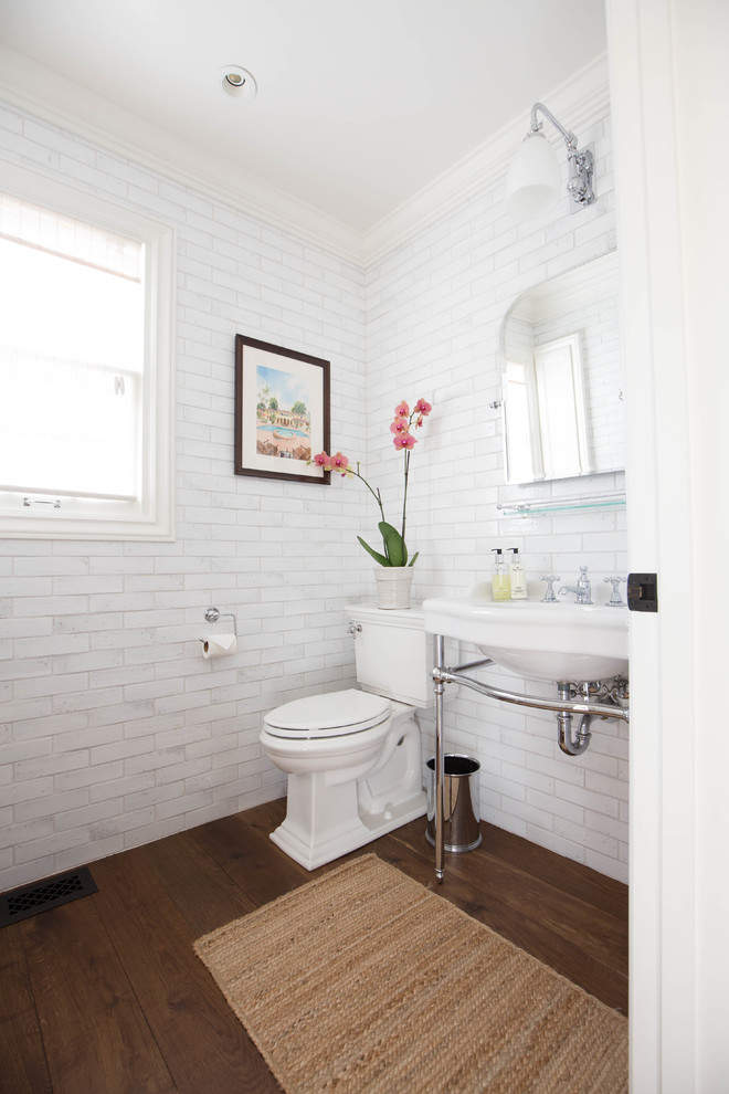 This is an example of a small classic cloakroom in San Diego with freestanding cabinets, a two-piece toilet, white tiles, white walls, dark hardwood flooring, a pedestal sink and brown floors.