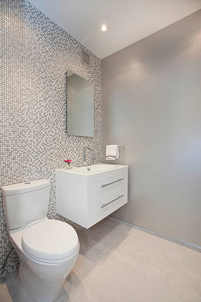 This is an example of a contemporary cloakroom in New York with flat-panel cabinets, white cabinets, a two-piece toilet, grey walls, multi-coloured tiles, mosaic tiles and light hardwood flooring.