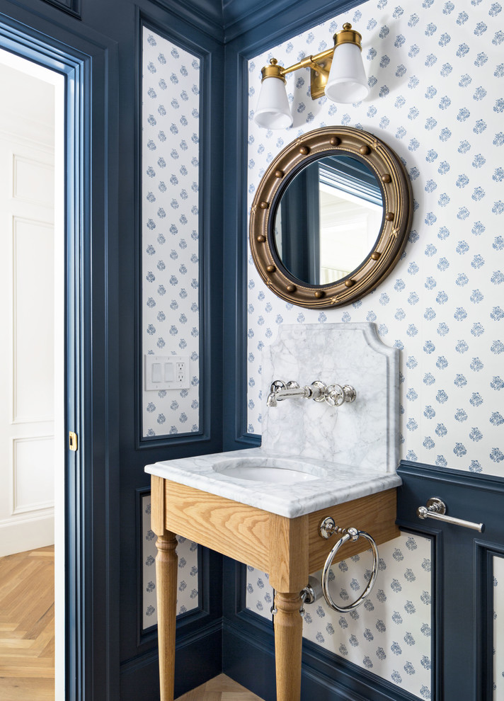 Diseño de aseo clásico con puertas de armario de madera clara, paredes azules, suelo de madera clara, lavabo tipo consola, suelo marrón y encimeras blancas