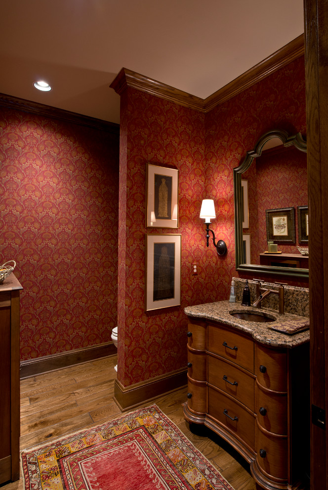 Mittelgroße Mediterrane Gästetoilette mit verzierten Schränken, hellbraunen Holzschränken, roter Wandfarbe, braunem Holzboden, Unterbauwaschbecken und Granit-Waschbecken/Waschtisch in Wichita