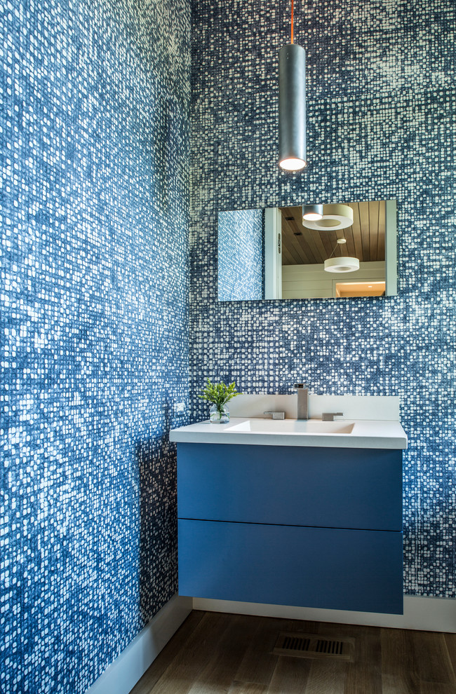 Foto på ett stort vintage vit toalett, med släta luckor, blå skåp, blå väggar, mellanmörkt trägolv, ett integrerad handfat och brunt golv