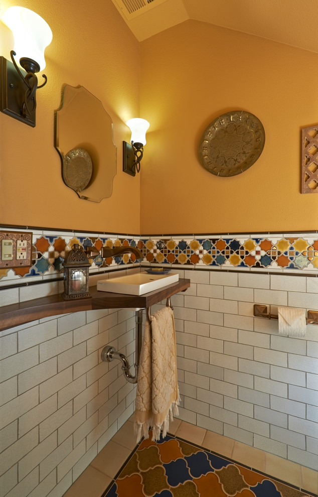 На фото: туалет в средиземноморском стиле с настольной раковиной, столешницей из дерева и разноцветной плиткой с