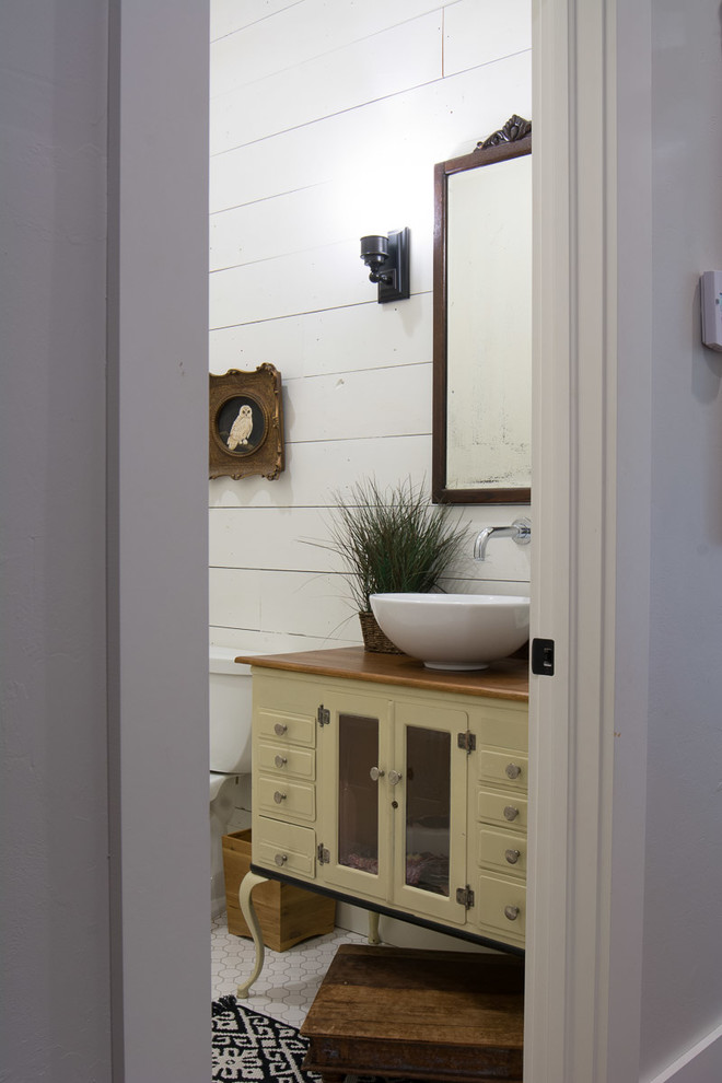 Photo of a medium sized rural cloakroom in Oklahoma City with freestanding cabinets, beige cabinets, a two-piece toilet, white walls, porcelain flooring, a vessel sink, wooden worktops and white floors.