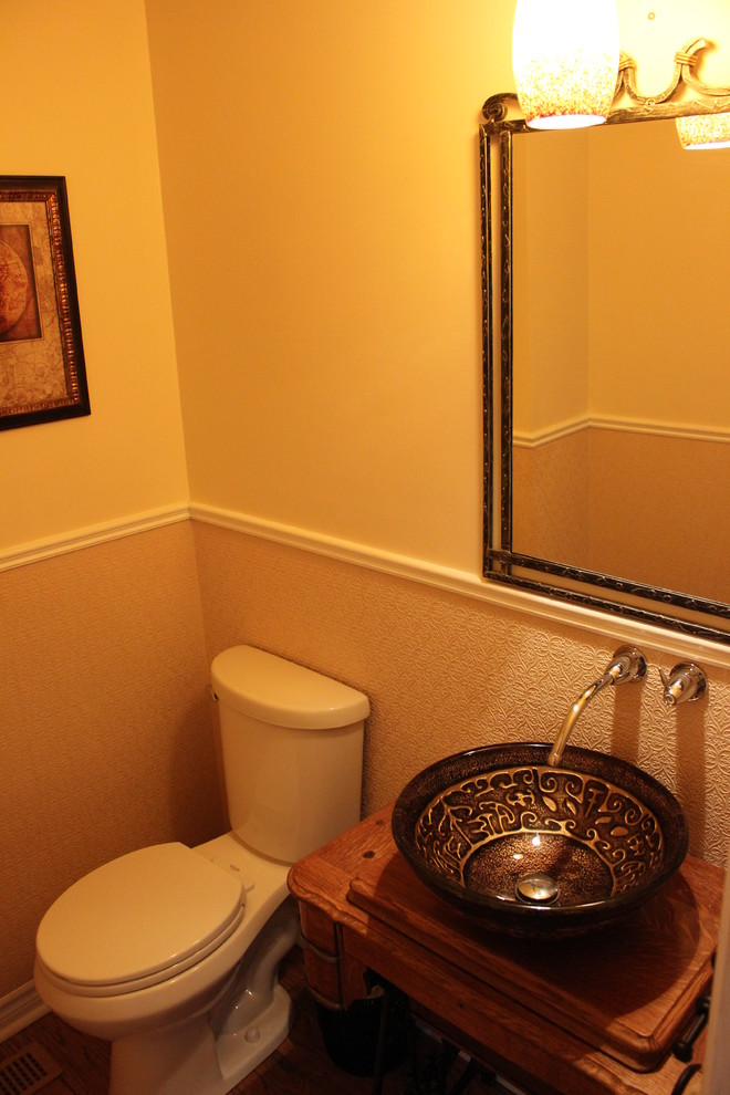 This is an example of a small classic cloakroom in Toronto with freestanding cabinets, medium wood cabinets, a two-piece toilet, beige walls, light hardwood flooring, a vessel sink and wooden worktops.