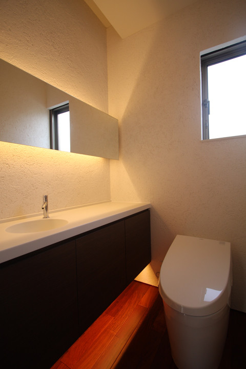 Идея дизайна: туалет в стиле модернизм с плоскими фасадами, темными деревянными фасадами, унитазом-моноблоком, белой плиткой, белыми стенами, темным паркетным полом, монолитной раковиной и коричневым полом