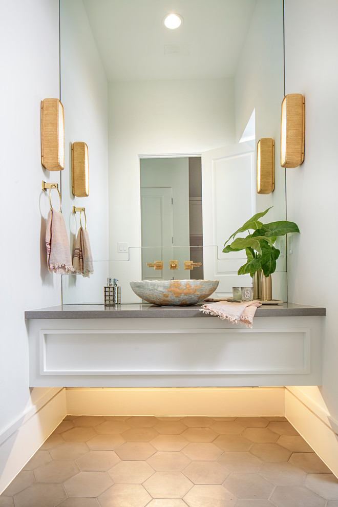 Modern inredning av ett stort toalett, med möbel-liknande, vita skåp, grå kakel, vita väggar, ett fristående handfat, marmorbänkskiva och cementgolv