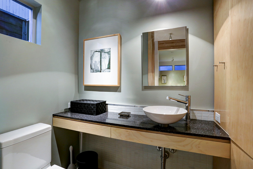 Стильный дизайн: маленький туалет в стиле модернизм с плоскими фасадами, светлыми деревянными фасадами, раздельным унитазом, белой плиткой, стеклянной плиткой, зелеными стенами, настольной раковиной, столешницей из искусственного камня и черной столешницей для на участке и в саду - последний тренд