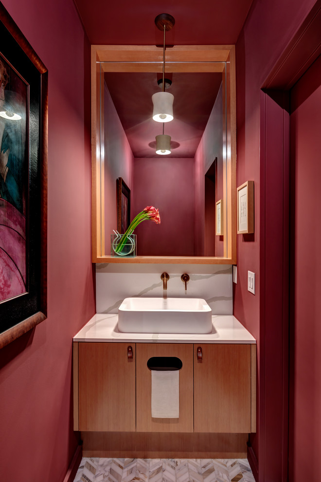 На фото: туалет в стиле модернизм с плоскими фасадами, светлыми деревянными фасадами, красными стенами, полом из мозаичной плитки, настольной раковиной, столешницей из искусственного кварца, белым полом и белой столешницей