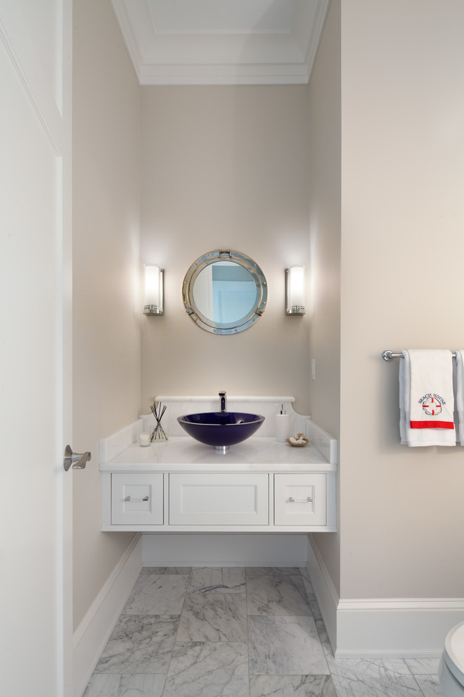 ワシントンD.C.にあるビーチスタイルのおしゃれなトイレ・洗面所 (ベッセル式洗面器、落し込みパネル扉のキャビネット、白いキャビネット、ベージュの壁、白い洗面カウンター) の写真
