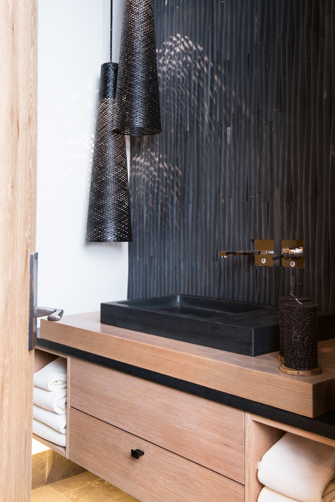 デンバーにあるコンテンポラリースタイルのおしゃれなトイレ・洗面所 (ベッセル式洗面器、フラットパネル扉のキャビネット、淡色木目調キャビネット、黒い壁) の写真