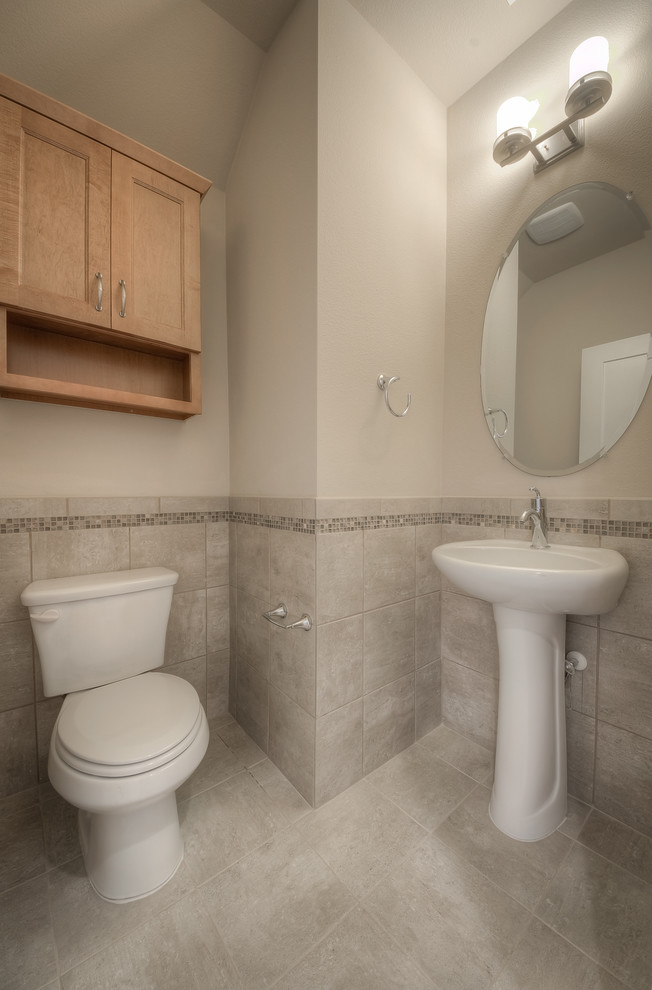 Photo of a small cloakroom in Austin with a pedestal sink, recessed-panel cabinets, light wood cabinets, a two-piece toilet, porcelain tiles, beige walls, porcelain flooring and grey tiles.