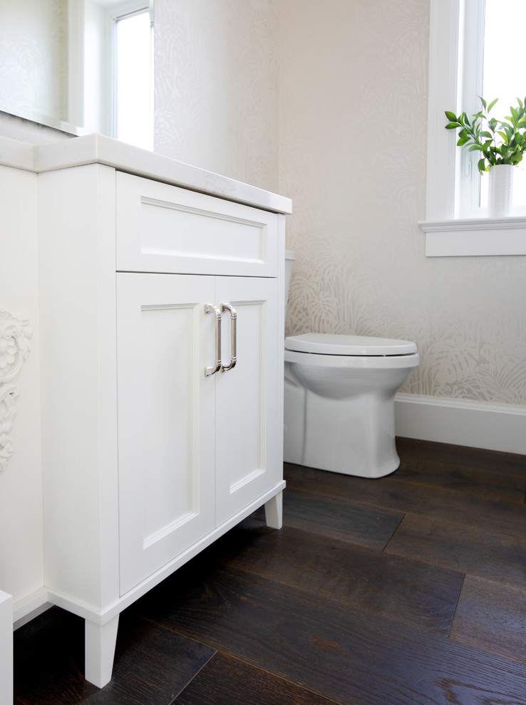 This is an example of a small beach style cloakroom in Vancouver with recessed-panel cabinets, white cabinets, a two-piece toilet, white walls, dark hardwood flooring, a submerged sink, engineered stone worktops, brown floors and white worktops.