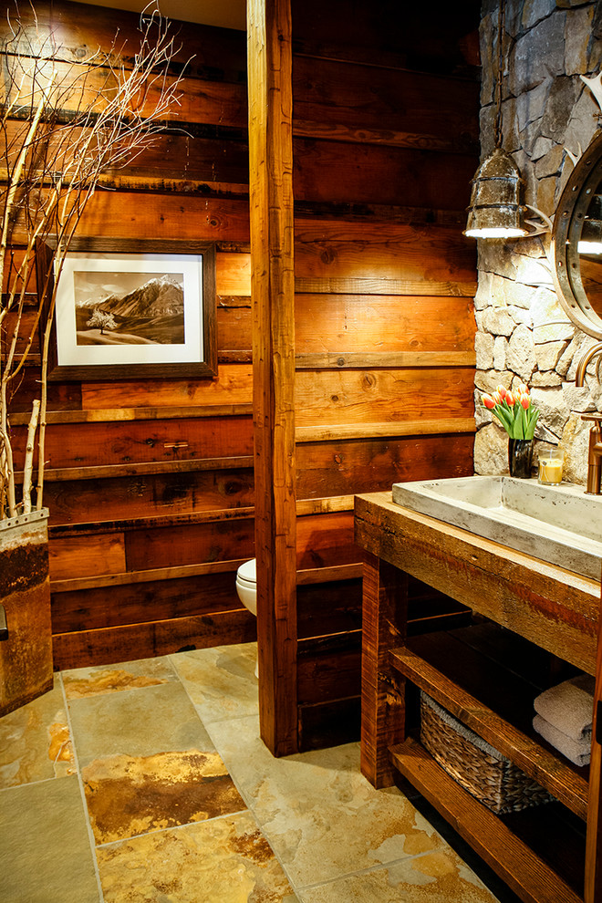 Exemple d'un WC et toilettes montagne de taille moyenne avec un carrelage gris, un carrelage de pierre, un mur marron, un sol en ardoise, un plan de toilette en bois et un plan de toilette marron.