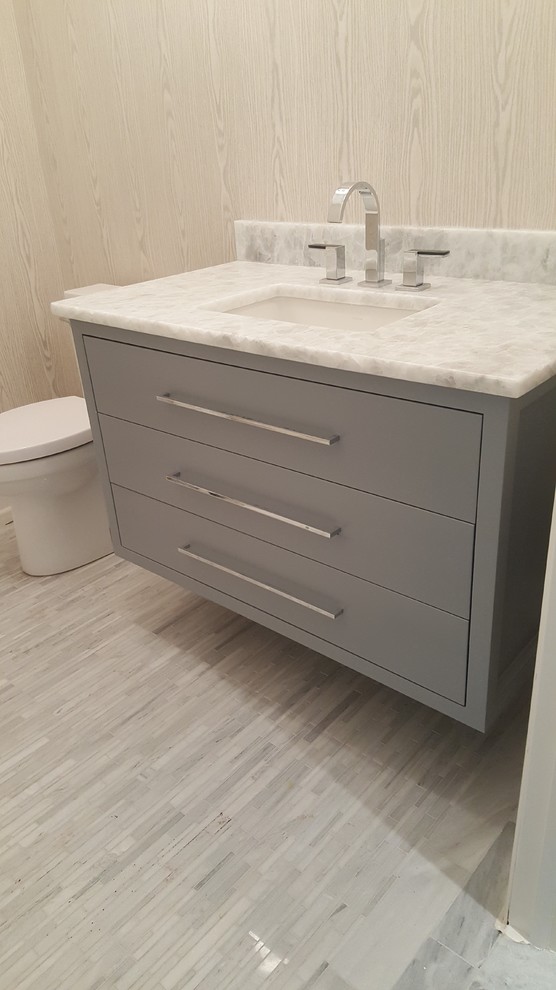 Medium sized modern cloakroom in New York with flat-panel cabinets, grey cabinets, a two-piece toilet, beige walls, porcelain flooring, a submerged sink, soapstone worktops, grey floors and white worktops.