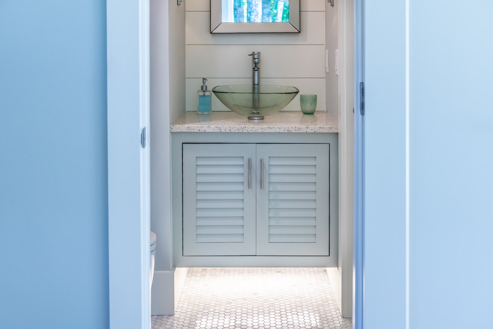 Modelo de aseo costero pequeño con armarios con puertas mallorquinas, suelo con mosaicos de baldosas, lavabo sobreencimera, encimera de vidrio reciclado y suelo blanco