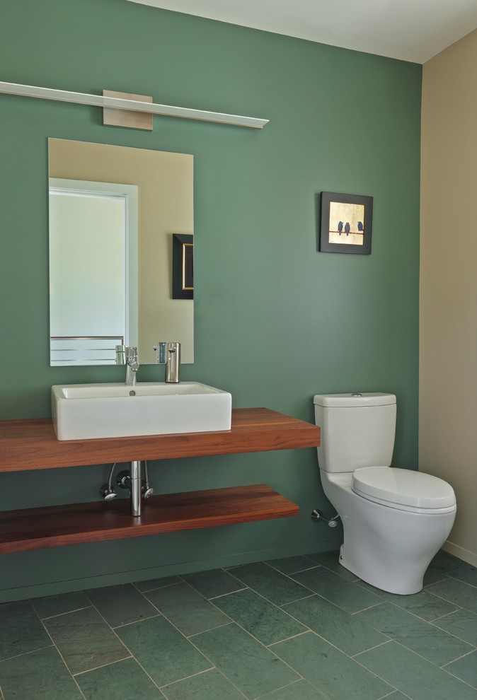 Exemple d'un WC et toilettes moderne en bois brun de taille moyenne avec un placard avec porte à panneau surélevé, WC séparés, un mur vert, un sol en ardoise, une vasque et un plan de toilette en bois.