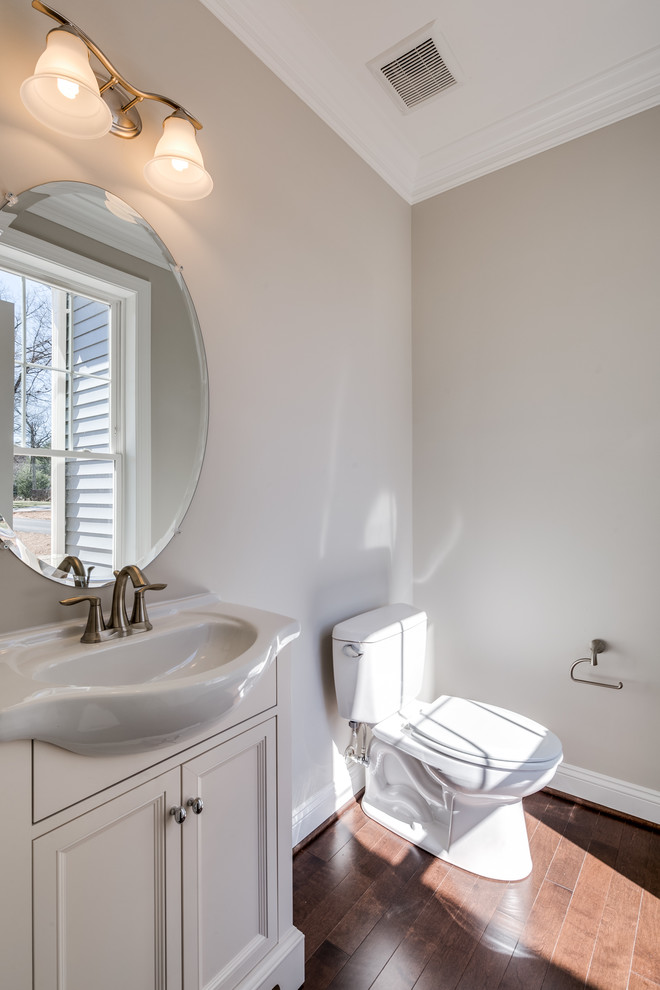 Inspiration för små klassiska toaletter, med luckor med infälld panel, vita skåp, en toalettstol med separat cisternkåpa, grå väggar, mellanmörkt trägolv, ett integrerad handfat, laminatbänkskiva och brunt golv