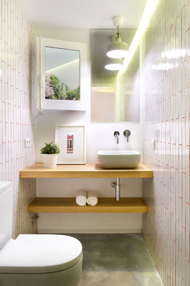 Inredning av ett medelhavsstil litet brun brunt toalett, med öppna hyllor, skåp i mellenmörkt trä, en toalettstol med separat cisternkåpa, rosa kakel, keramikplattor, betonggolv, ett fristående handfat, träbänkskiva och vita väggar