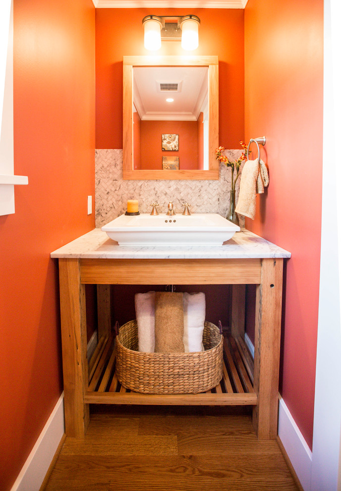 Bild på ett litet amerikanskt toalett, med möbel-liknande, skåp i ljust trä, en toalettstol med separat cisternkåpa, vit kakel, mosaik, orange väggar, mellanmörkt trägolv, ett fristående handfat, bänkskiva i kvarts och brunt golv