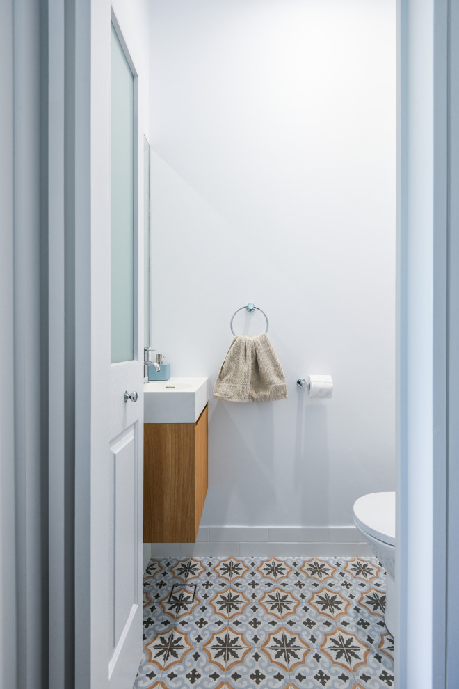 Cette photo montre un petit WC et toilettes moderne en bois brun avec un placard à porte plane, un carrelage blanc, des carreaux de céramique, un mur blanc, un sol en carrelage de céramique, un lavabo intégré, un plan de toilette en quartz modifié, un sol bleu, un plan de toilette blanc et meuble-lavabo suspendu.