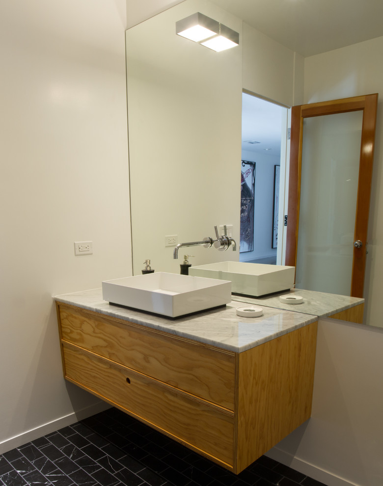 Photo of a medium sized modern cloakroom in Los Angeles with flat-panel cabinets, light wood cabinets, white walls, a vessel sink and marble worktops.