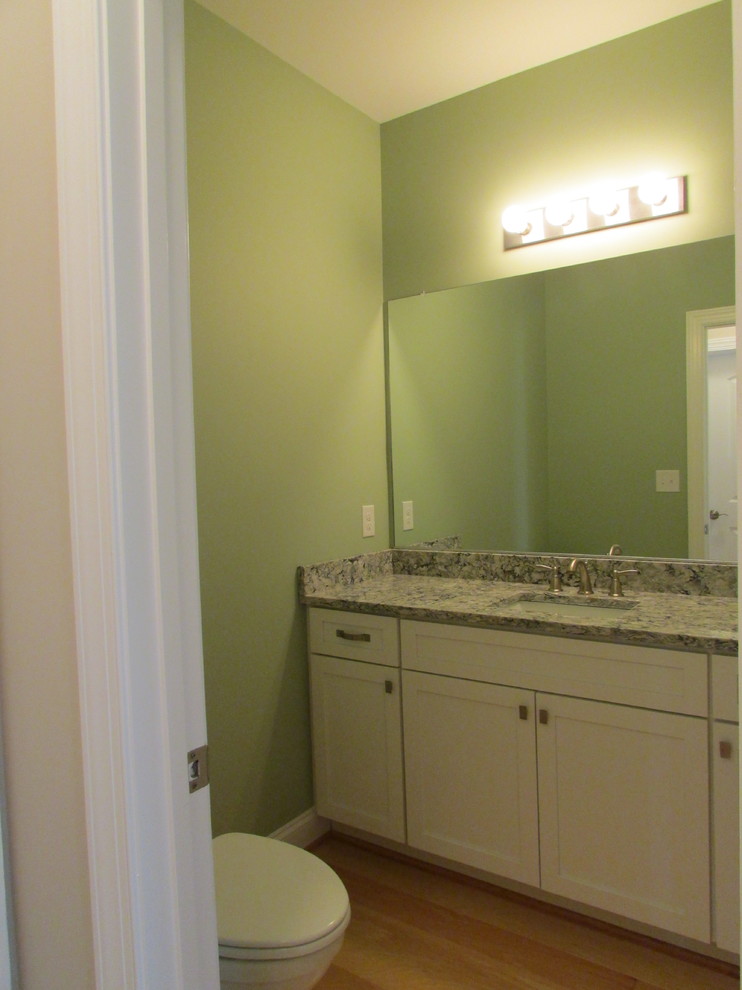 Cette photo montre un WC et toilettes chic de taille moyenne avec un placard avec porte à panneau encastré, des portes de placard blanches, WC séparés, un mur vert, parquet clair, un lavabo encastré et un plan de toilette en quartz modifié.