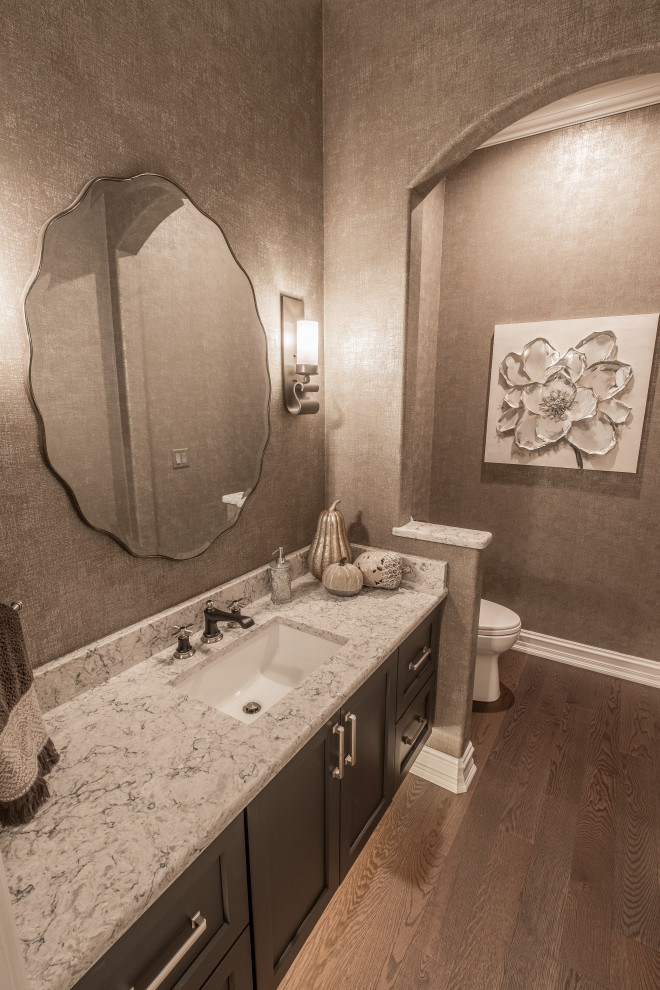 Cette image montre un grand WC et toilettes rustique avec un placard avec porte à panneau encastré, des portes de placard marrons, parquet foncé, un lavabo encastré, un sol marron, un plan de toilette gris, meuble-lavabo suspendu et du papier peint.