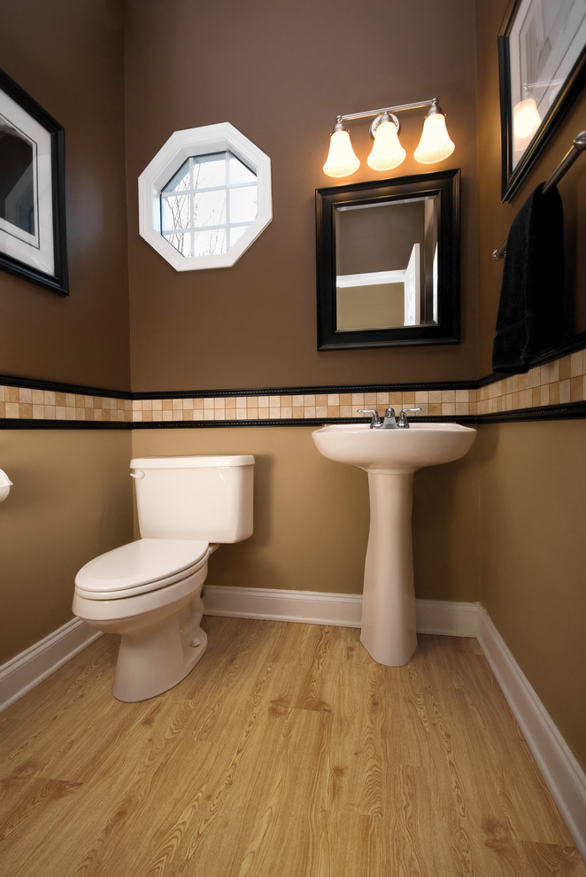 Example of a small trendy beige tile and ceramic tile light wood floor powder room design in Other with a two-piece toilet, brown walls and a pedestal sink