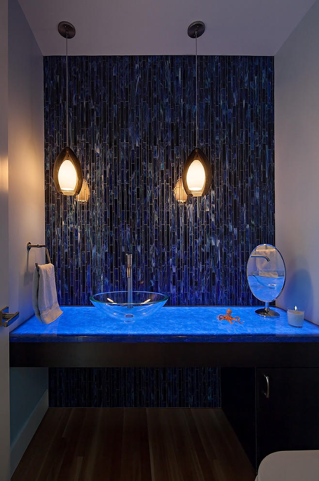 Photo of a contemporary cloakroom in Seattle with a vessel sink, flat-panel cabinets, dark wood cabinets, glass worktops, a one-piece toilet, blue tiles, medium hardwood flooring and matchstick tiles.