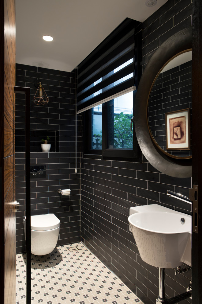 Asiatisk inredning av ett toalett, med en vägghängd toalettstol, svart kakel, svarta väggar, ett väggmonterat handfat och vitt golv
