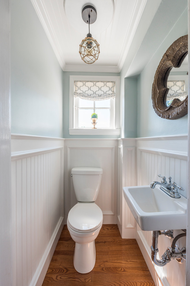 Inredning av ett klassiskt litet toalett, med en toalettstol med separat cisternkåpa, blå väggar, mellanmörkt trägolv, ett väggmonterat handfat och brunt golv