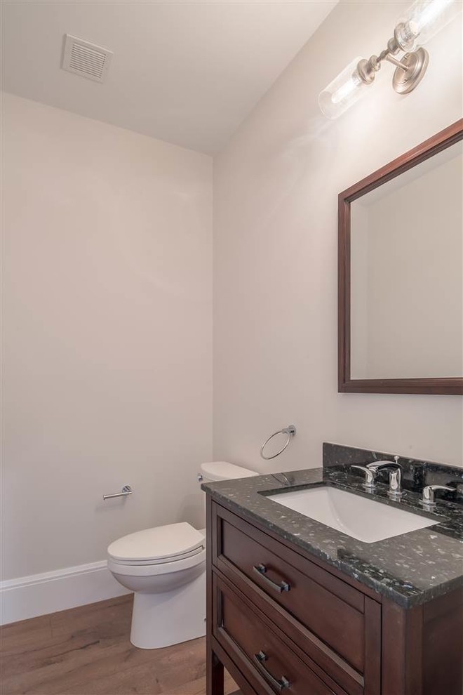 Amerikansk inredning av ett litet svart svart toalett, med möbel-liknande, skåp i mörkt trä, beige väggar, mellanmörkt trägolv, ett undermonterad handfat och bänkskiva i kvartsit