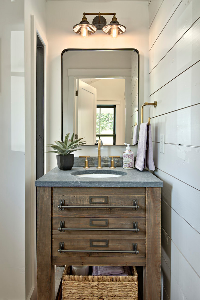 Diseño de aseo campestre con armarios tipo mueble, puertas de armario de madera en tonos medios, paredes blancas, lavabo bajoencimera y encimeras grises