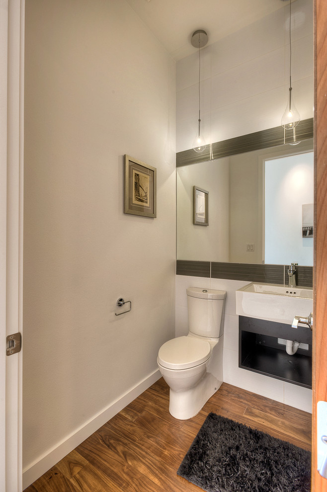 На фото: туалет в стиле модернизм с настольной раковиной, открытыми фасадами, темными деревянными фасадами, раздельным унитазом, серой плиткой, стеклянной плиткой, серыми стенами и паркетным полом среднего тона с