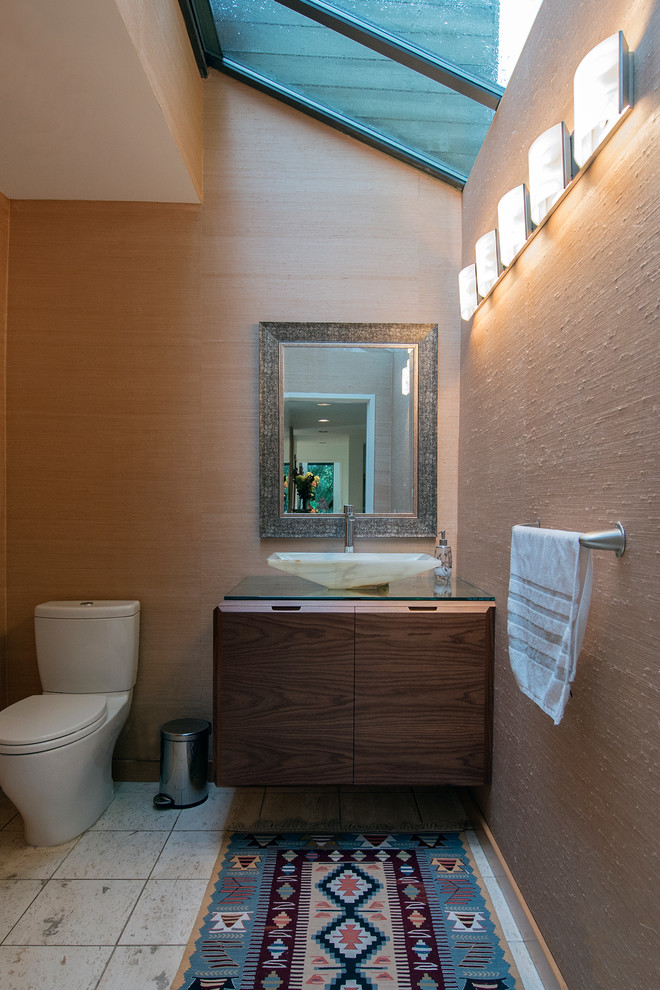 Example of a mid-sized minimalist travertine floor and white floor powder room design in Vancouver with flat-panel cabinets, dark wood cabinets, a two-piece toilet, beige walls, a vessel sink and glass countertops