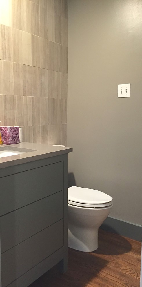 Cette photo montre un petit WC et toilettes moderne avec un lavabo encastré, un placard à porte plane, des portes de placard grises, un plan de toilette en quartz modifié, un carrelage gris, un carrelage de pierre, un mur gris et un sol en bois brun.