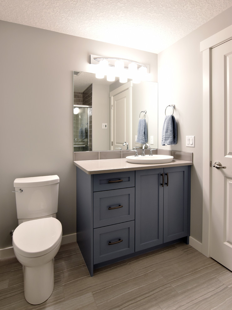 Idée de décoration pour un WC et toilettes tradition de taille moyenne avec un placard à porte shaker, des portes de placard bleues, WC séparés, un mur gris, un sol en carrelage de porcelaine, une vasque, un plan de toilette en granite et un sol gris.