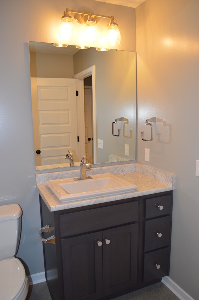 Exemple d'un petit WC et toilettes craftsman en bois foncé avec un placard à porte shaker, WC à poser, un mur gris, un sol en linoléum, un lavabo posé et un plan de toilette en stratifié.