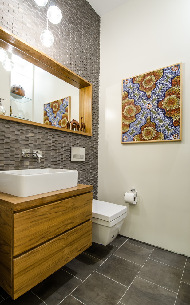 Idées déco pour un WC suspendu contemporain en bois brun de taille moyenne avec un placard à porte plane, un plan de toilette en bois, un carrelage gris, un mur blanc, un sol en carrelage de porcelaine et une vasque.