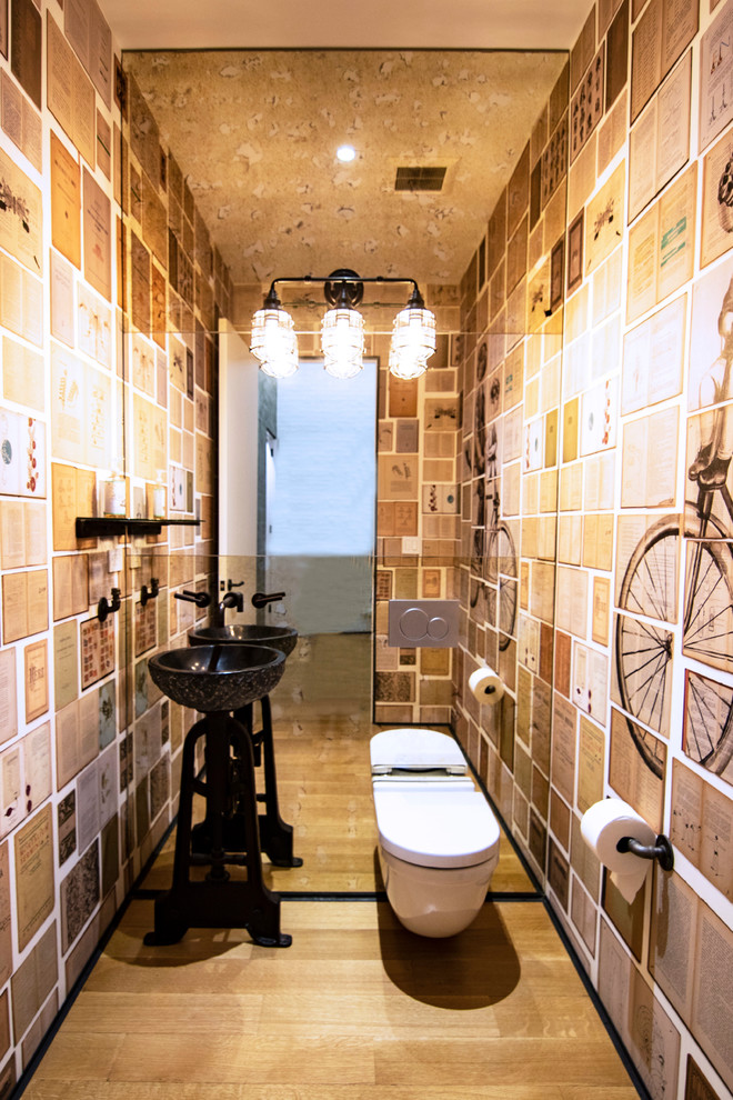 Пример оригинального дизайна: большой туалет в стиле лофт с инсталляцией, разноцветными стенами, светлым паркетным полом, настольной раковиной, мраморной столешницей, коричневым полом и черной столешницей