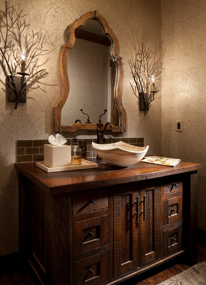 На фото: туалет в стиле рустика с настольной раковиной, темными деревянными фасадами, столешницей из дерева, коричневой плиткой и коричневой столешницей с