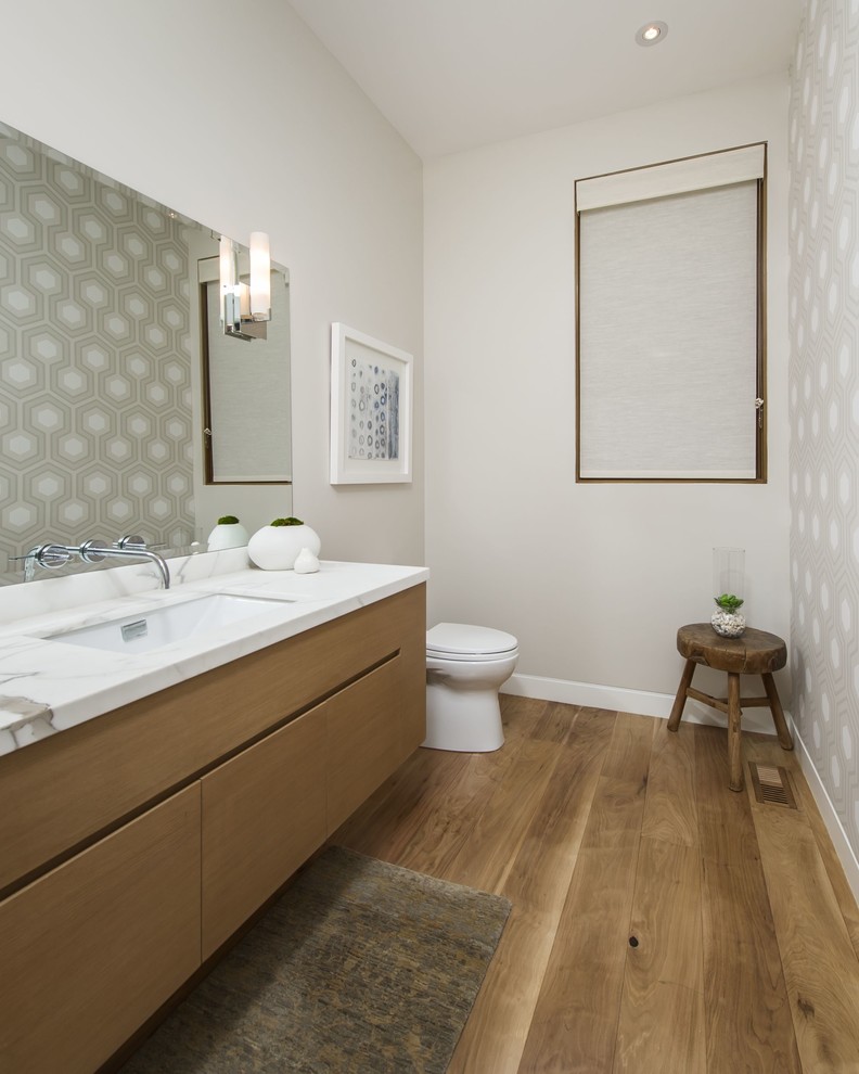 Inspiration pour un grand WC et toilettes design en bois brun avec un lavabo encastré, un placard à porte plane, un plan de toilette en marbre, WC à poser, un mur beige, un sol en bois brun et un plan de toilette blanc.