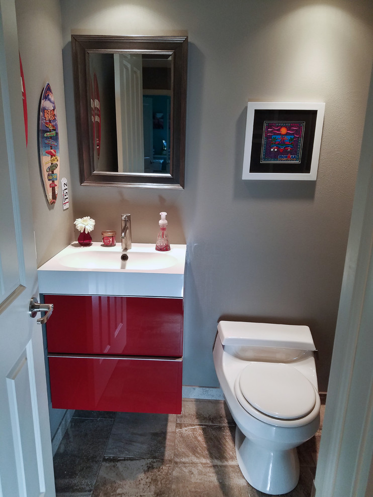 Cette photo montre un petit WC et toilettes tendance avec un placard à porte plane, des portes de placard rouges, WC à poser, un carrelage marron, des carreaux de porcelaine, un mur gris, un sol en carrelage de porcelaine, un lavabo intégré et un plan de toilette en surface solide.