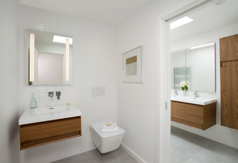 Inspiration for a small modern cloakroom in Boston with flat-panel cabinets, medium wood cabinets, a wall mounted toilet, white tiles, porcelain tiles, white walls, porcelain flooring, an integrated sink, grey floors, white worktops and a floating vanity unit.