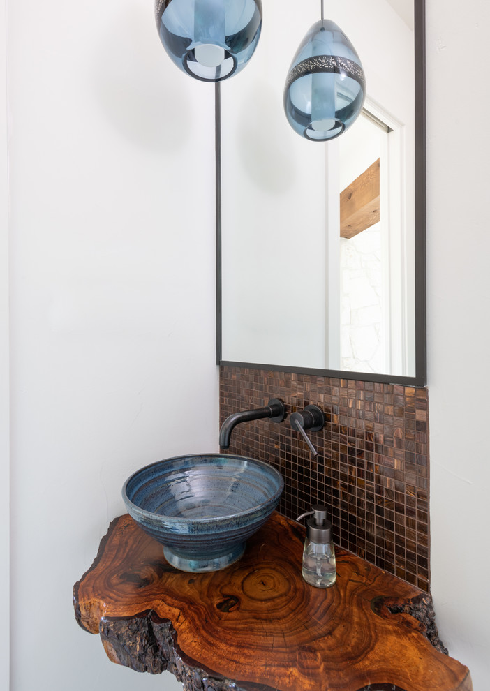 Inspiration for a mid-sized southwestern brown tile and mosaic tile powder room remodel in Austin with white walls, a vessel sink, wood countertops and brown countertops