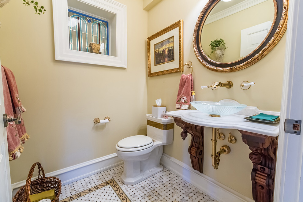 На фото: туалет в классическом стиле с унитазом-моноблоком, бежевыми стенами, полом из мозаичной плитки, настольной раковиной и разноцветным полом с