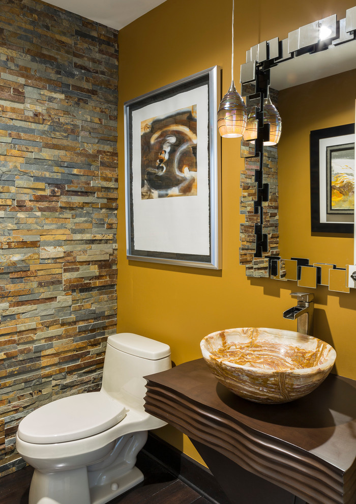 Cette image montre un WC et toilettes design avec WC à poser, un carrelage multicolore, un carrelage de pierre, un mur jaune, parquet foncé, une vasque, un plan de toilette en bois et un plan de toilette marron.